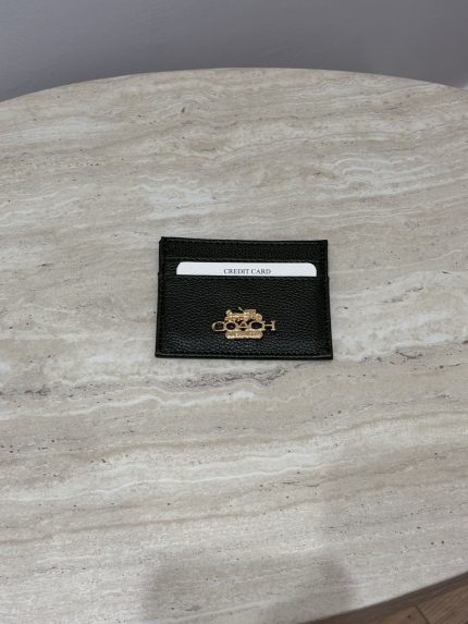 Black Coach cardholder with gold logo on marble surface.