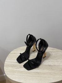 Black YSL Opyum sandals with gold heels on table.