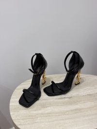 Black YSL Opyum sandals with gold logo heels on table.