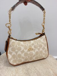 Coach handbag with gold chain and logo pattern on table.