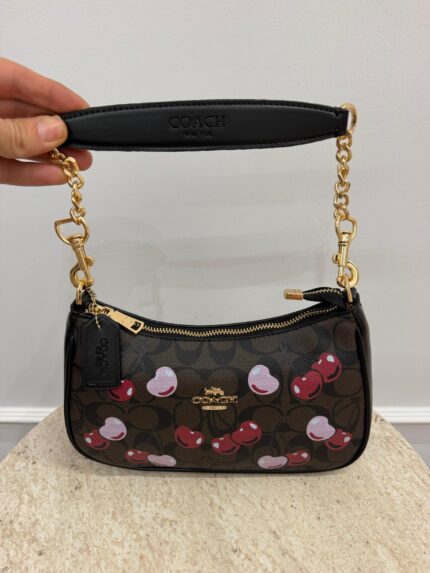 Coach cherry handbag with gold chain and logo design.