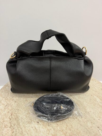 Black Polène leather handbag with strap on beige surface.