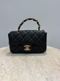 Chanel Mini Flap bag with gold chain handle on marble surface.