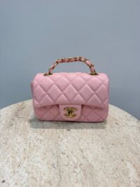 Pink Chanel Mini Flap bag with gold chain handle on marble surface.