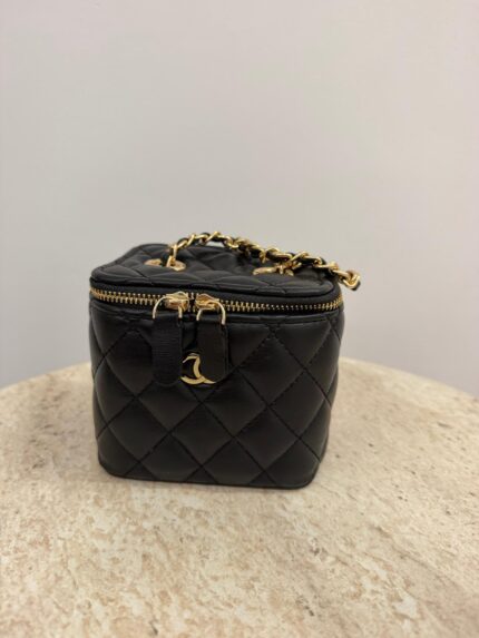 Chanel Vanity Mini black quilted bag with gold chain on table.